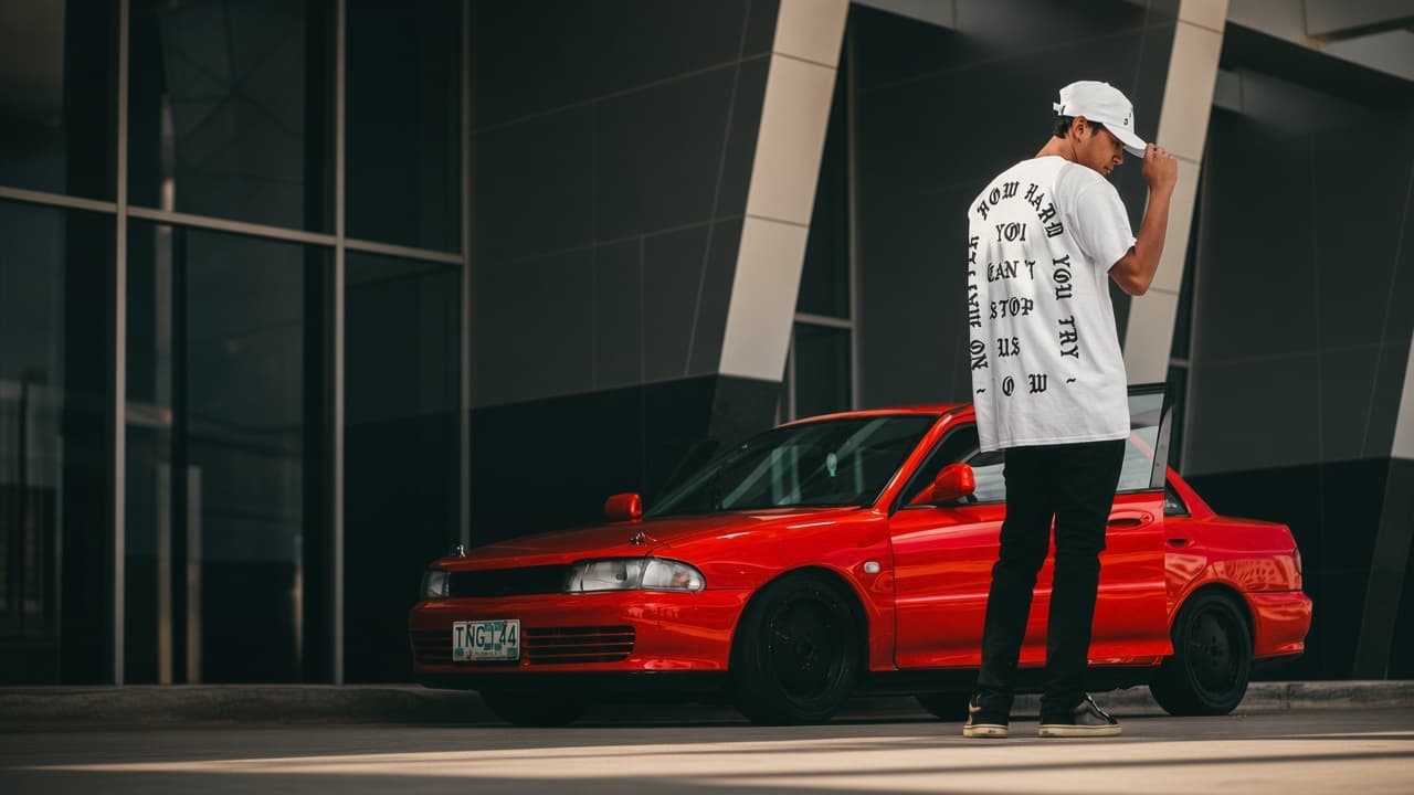 Back of the white Can't Stop Us Tee, worn beside a red Lancer in a Cebu City car park